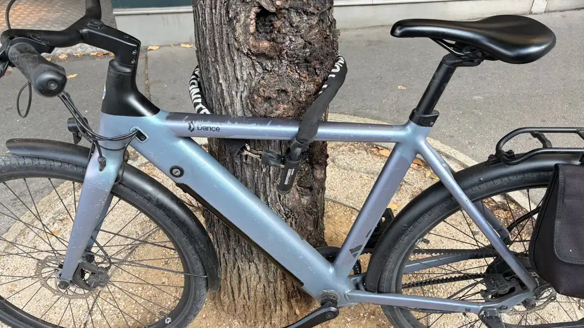 Dance One high-frame e-bike locked to a tree with a sleeved Kryptonite combination chain lock, battery integrated in the down tube